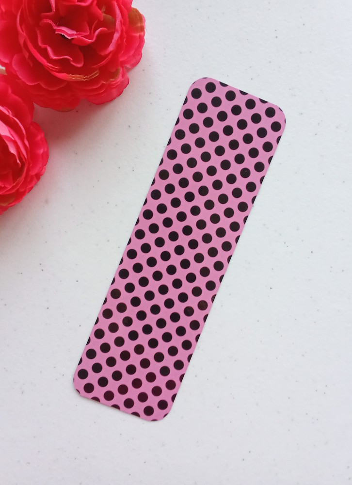 Marcapáginas con diseño de círculos. Laminado, impreso a doble cara, esquinas redondeadas. Círculos negros sobre fondo rosa.