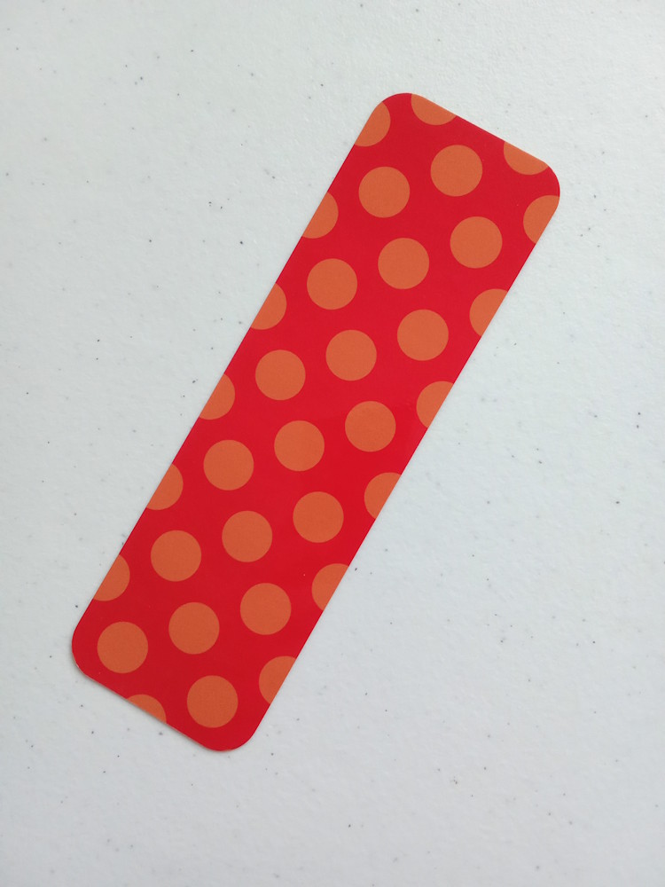 Marcapáginas con diseño de círculos medianos. Laminado, impreso a doble cara, esquinas redondeadas. Círculos naranjas sobre fondo rojo.